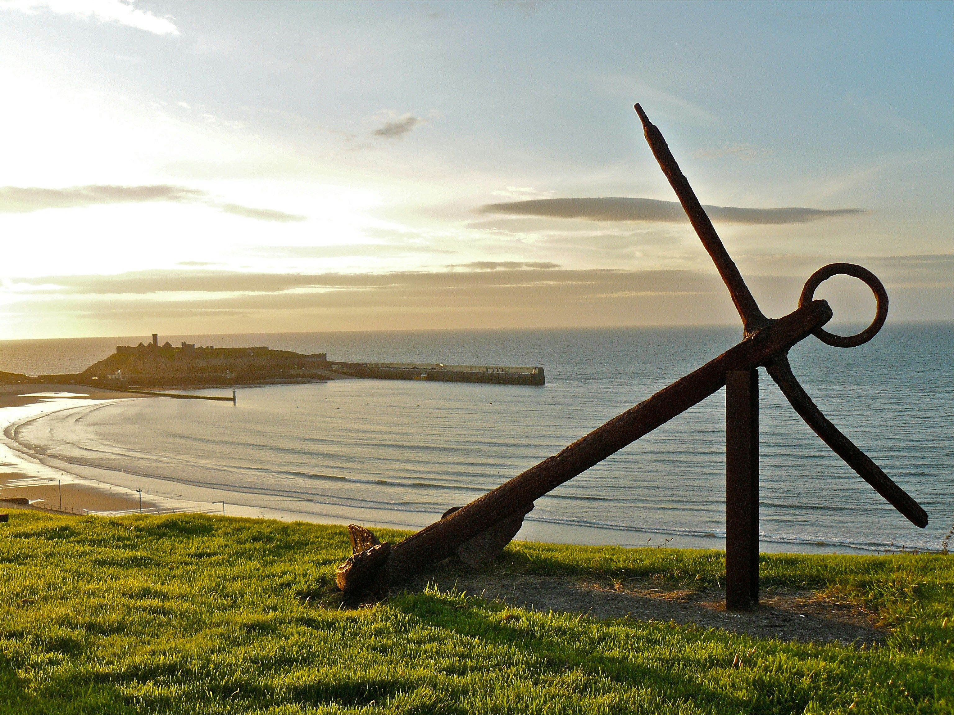 Looking out to sea over Peel Beach and Peel Castle, a rusted boat anchor sits on grass